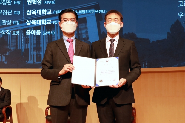 삼육대 재무실 권혁성(오른쪽) 과장과 김일목 총장이 표창장을 들고 기념사진을 찍고 있다..